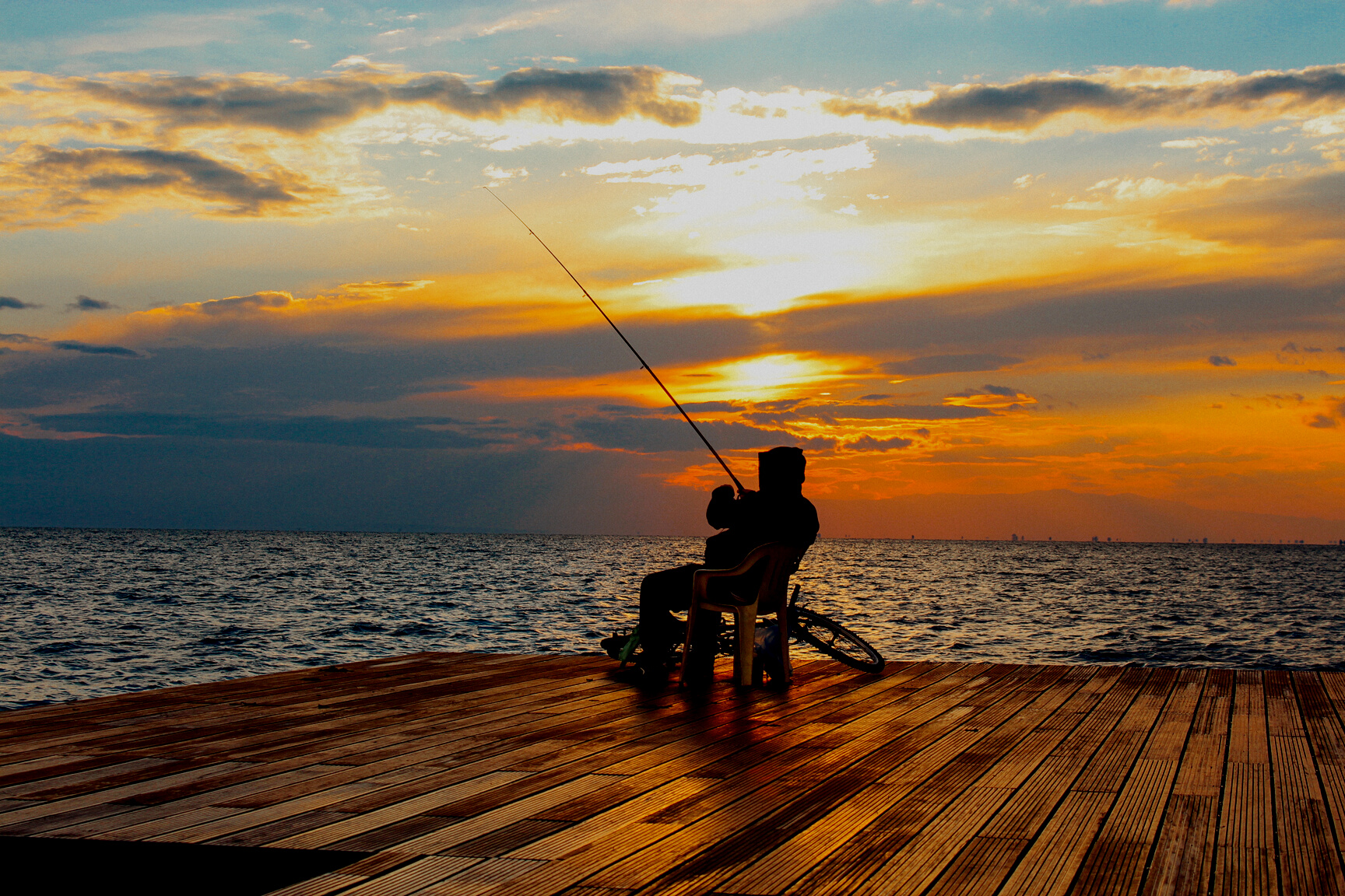 Silhouette of Person Sitting on Chair Holding Fishing Rod Near Body of Water during Golden Hour